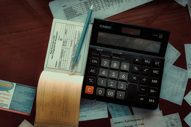 A calculator on a desk covered in receipts